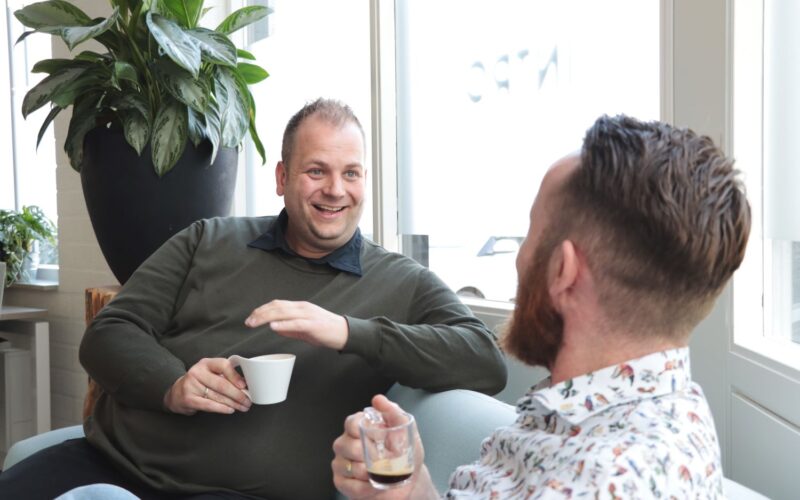 twee mannen zijn op kantoor een bakje koffie aan het drinken en ondertussen aan het overleggen.